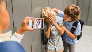 Schoolchildren cruel boys filming on the phone torturing bullying their classmate in school hall. Puberty difficult age